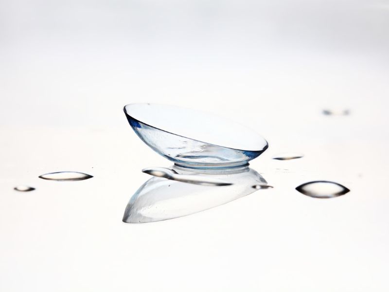 Soczewka kontaktowa na tle z kroplami płynu – dobór soczewek w Optosferze w Warszawie